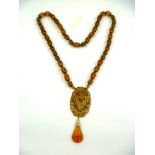 A 1930's AMBER GLASS SAUTOIR with cast gilt metal pendant of a profile of a mystic, 82cm long