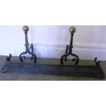 A PAIR OF WROUGHT IRON FIRE DOGS with brass ball finials and a cast iron decorative FIRE KERB, 112cm