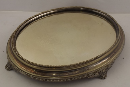 AN OVAL EPNS CAKE STAND, having mirror base, beaded surround, and raised on four cast scroll feet,