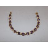 AN AMETHYST MOUNTED GOLD COLOURED METAL SET BRACELET, having fifteen stones and snap clasp,