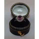 A RUBY AND DIAMOND CLUSTER RING, having oval central stone bordered by twelve brilliants, on plain