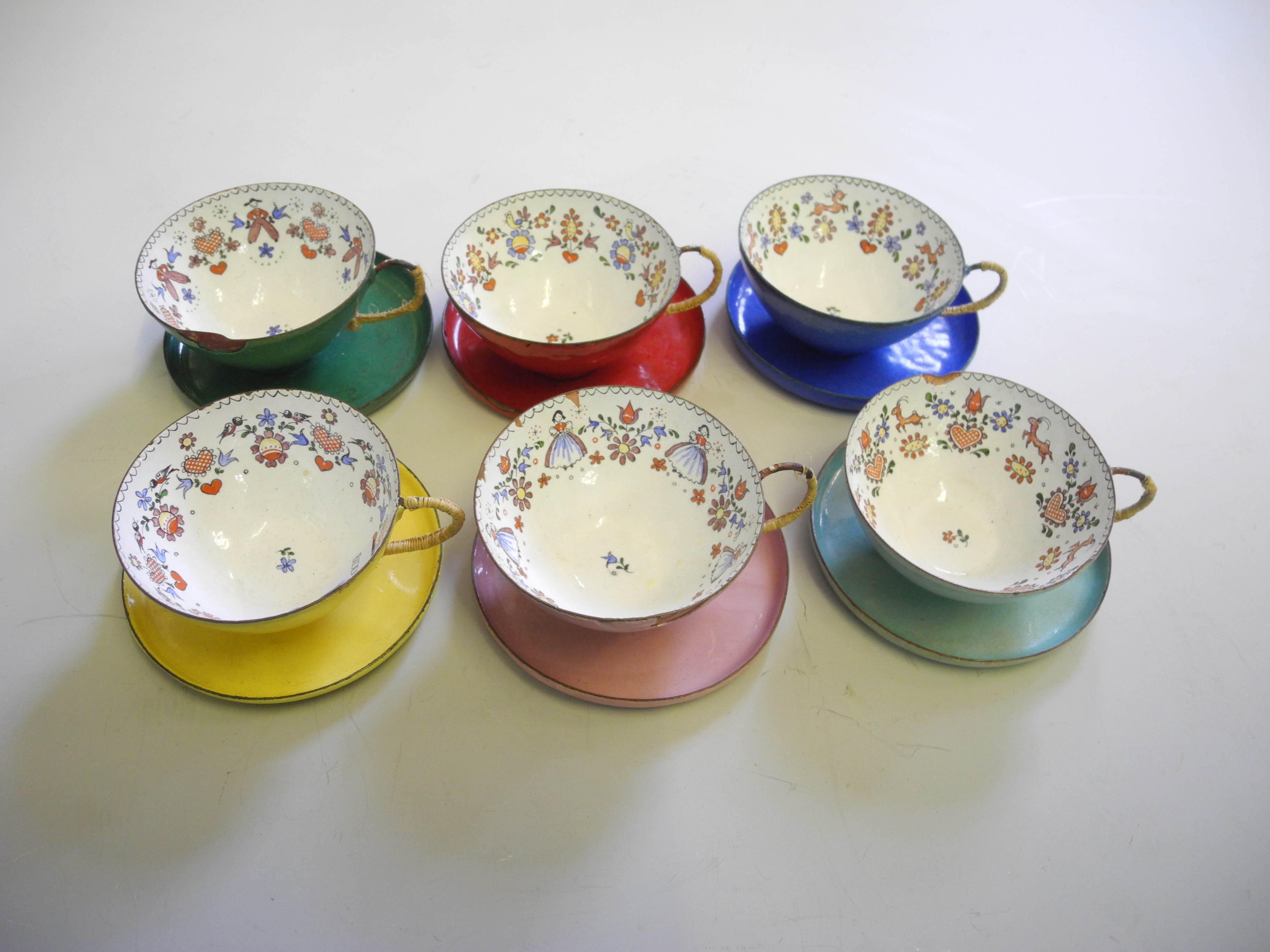 A group of six various coloured Austrian copper and enamel cups and saucers.