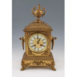 An early 20th Century brass mantel clock with ornate scroll decoration to body on four scroll feet