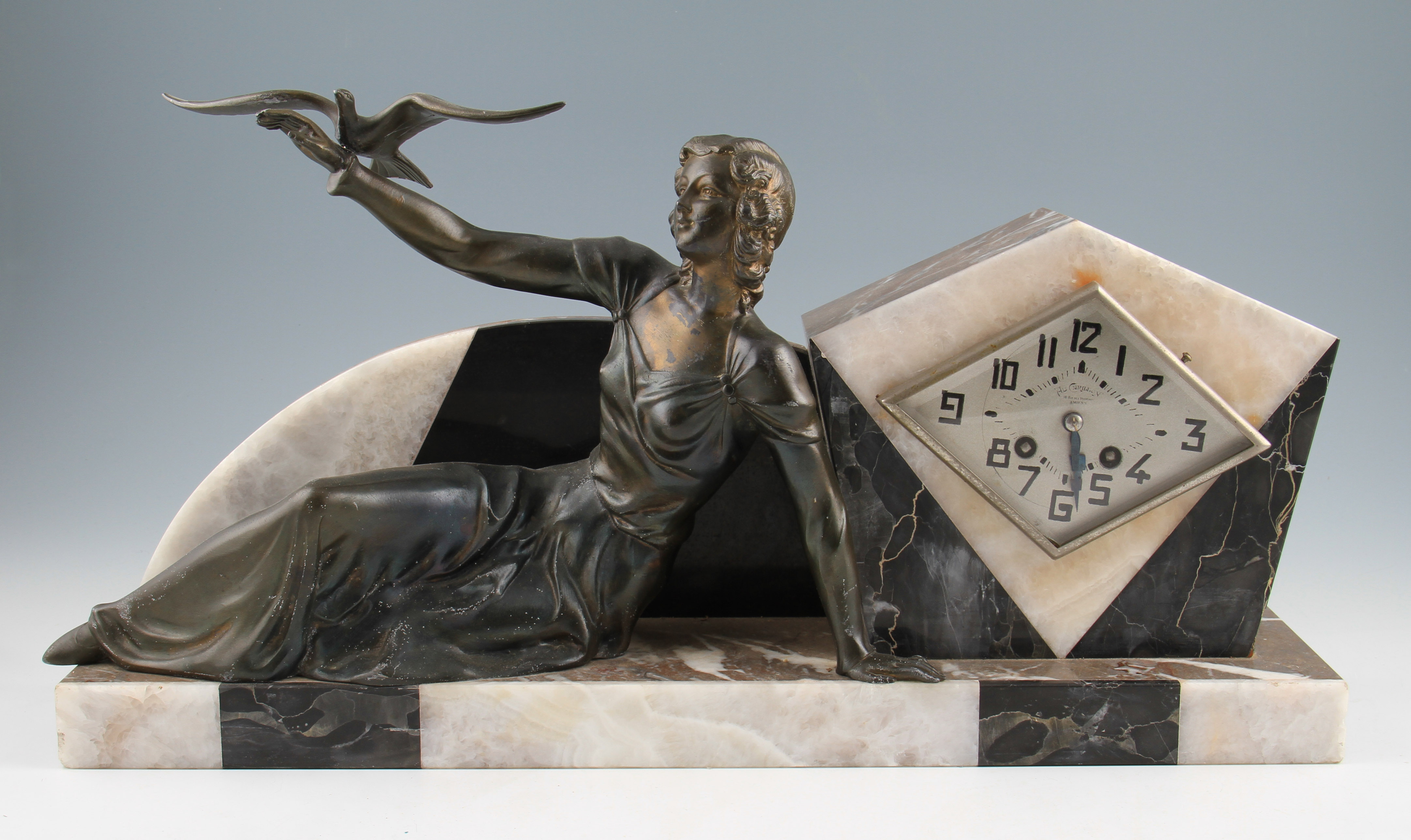 A French Art Deco mantle clock, depicting a seated bronzed spelter female reclining figure, a bird