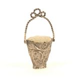 A silver pincushion (unmarked) in the form of a scroll and floral decorated basket, with swing '