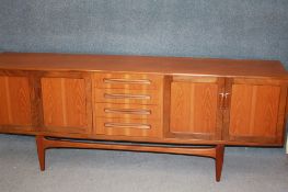 A teak sideboard with four central drawers flanked by two cupboard doors to each end supported on
