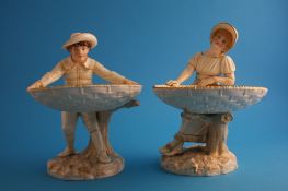 A pair of Royal Worcester comports modelled as a boy and girl holding two large woven baskets, green