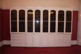 A large painted pine breakfront bookcase with moulded cornice below eight arched and glazed doors
