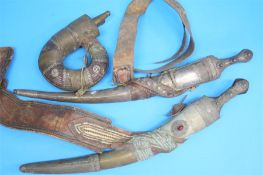 Two Middle Eastern daggers with decorative scabbards and leather belts, and a metalwork powder horn.