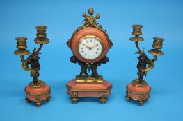 A small French clock garniture, the clock with enamelled circular dial supported by two putti and