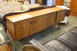 A long Teak sideboard with four drawers and three cupboard doors supported on turned legs.  206 cm