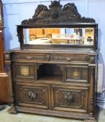 An early 20th century heavily carved oak cabinet with carved and mirrored raised back, below two