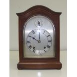 A mahogany mantle clock, arched top, with Roman numeral dial. 11 inches high.