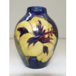 Moorcroft pottery bud vase of small proportion, tube-lined in the Hibiscus pattern against a blue