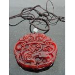 A Red Jadeite Pendant carved with Dragon and Icons strung on Black Silk