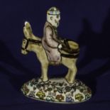 A porcelain figure group of a man riding backwards on a donkey