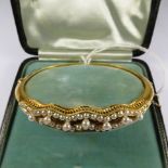 A late 19th century yellow gold hinged bangle with seed pearls set to the front section, fitted case