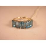 A silver ring set with five emerald cut blue topaz stones