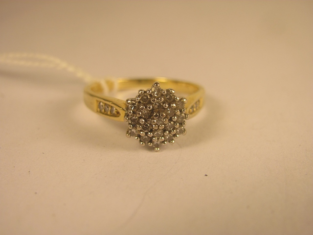 A contemporary 18ct yellow gold brilliant cut diamond cluster ring with diamond set shoulders