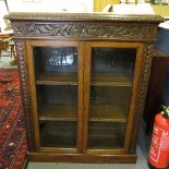 A late 19th century oak carved and glazed display bookcase