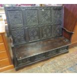 An 18th Century oak Settle, the sloped back with eight carved panels, hinged replacement seat