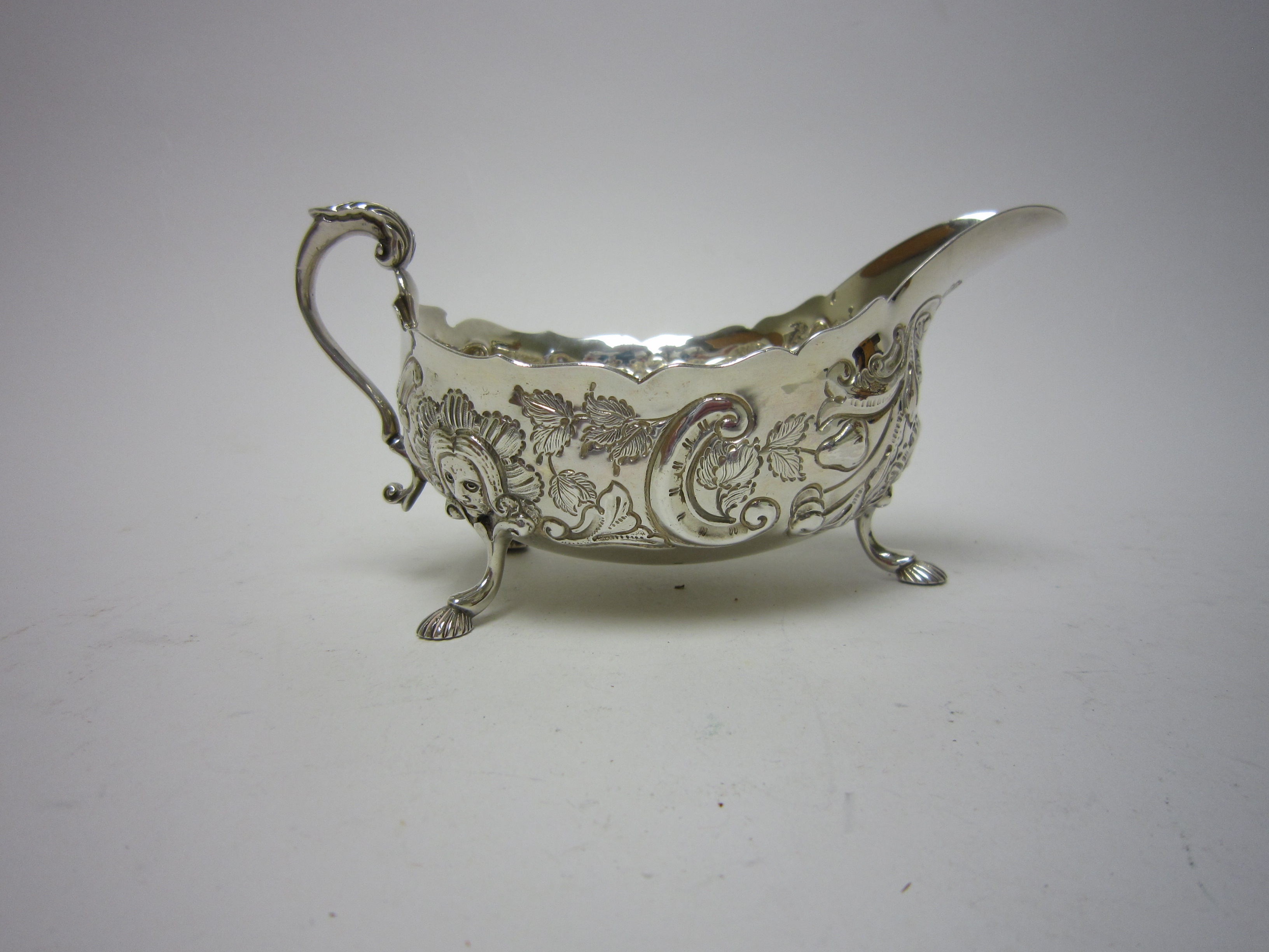 A modern heavy Irish silver Sauce Boat with floral and scroll embossing on mask supports and hoof