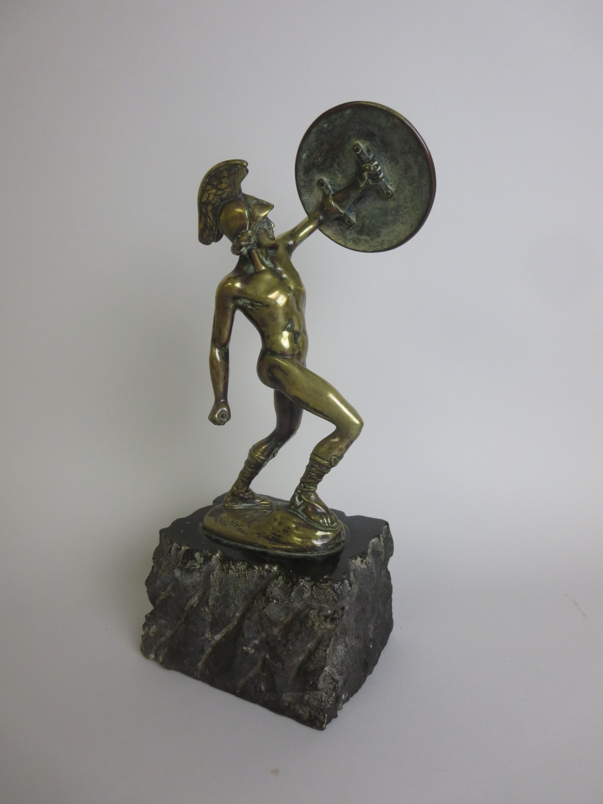 A bronze Figure of a Gladiator with raised circular shield, mounted upon stone base, signed R.