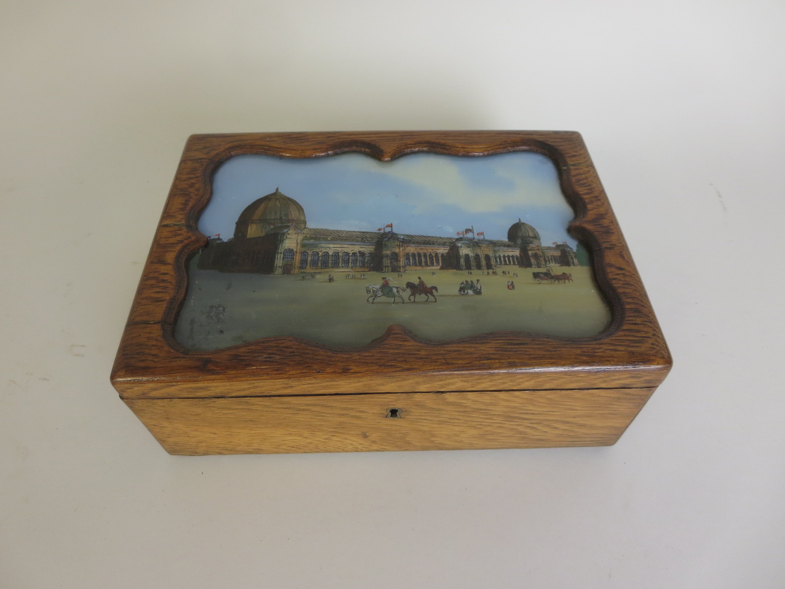 An oak Box, the hinged lid with inset painted panel of Paris Exhibition within shaped frame, 9 1/2in