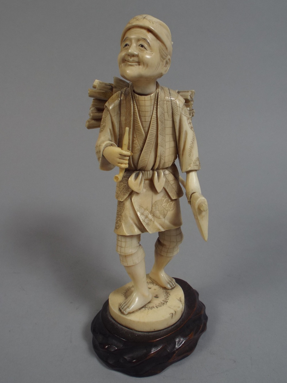 An Early 20th Century Ivory Okimono Figure of an Elderly Wood Cutter Holding an Axe and Pipe.