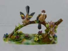 A Crown Staffordshire figure group of two birds sitting on a flowering tree branch, set on a rounded