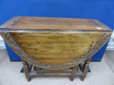 An Edwardian oval oak drop leaf table having carved decoration to the edge of the top, est. diameter