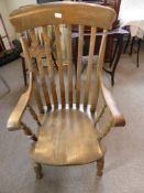 An antique low seated oak kitchen armchair having a slatted back on turned legs and stretchers.