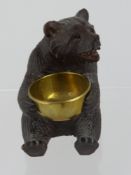 A Black Forest Bear depicted seated, holding a brass basin in its paws together with a carved