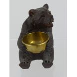 A Black Forest Bear depicted seated, holding a brass basin in its paws together with a carved