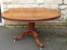 An Edwardian Mahogany Oval Tilt Top Table, the table on carved scroll feet with porcelain casters.