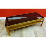 A retro teak coffee table having a smoked glass insert raised on moulded supports, 113 x 36cm