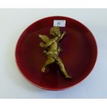 Red glazed pottery wall charger surmounted by a gilt metal cherub, 23cm wide