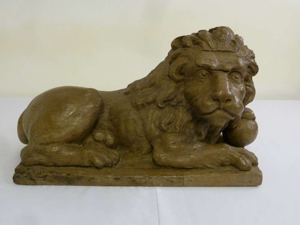 Wooden carving of a recumbent lion supporting a sphere