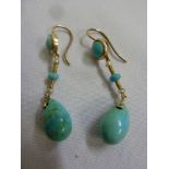 A pair of gold earrings set with turquoise drops