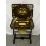 A Victorian ebonised Chinoiserie sewing table hinged cover on scrolling supports