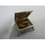 A miniature silver musical box, rectangular with hinged cover on four ball feet, fully import
