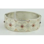 A gold inlaid silver hinged bangle,
set with small garnets.