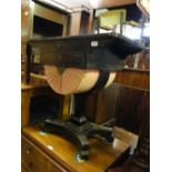 A Victorian ebonised sewing table with drawer and sliding basket under, on platform base.