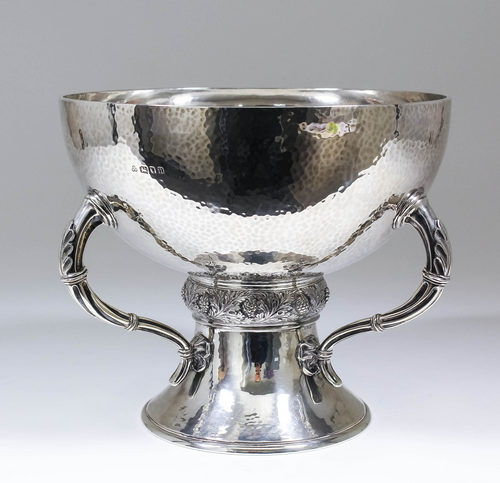 A George V hammered silver circular fruit bowl with three leaf capped and fluted handles, embossed