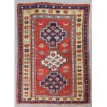 An antique Caucasian rug woven in colours with three stepped medallions on a madder ground within