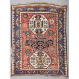 An antique Kazak rug woven in primary colours with three geometric medallions and filler motifs on a