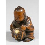 A Japanese boxwood netsuke, carved in the form of a seated boy opening fruit, 1.5ins (37mm) high,