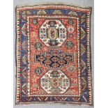 An antique Kazak rug woven in primary colours with three geometric medallions and filler motifs on a