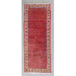 A modern Meshed runner woven in colours with numerous small boteh, on a red ground within stylised