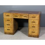 A 1930's walnut kneehole desk of Art Deco design with recessed centre, brown leather inset to top,